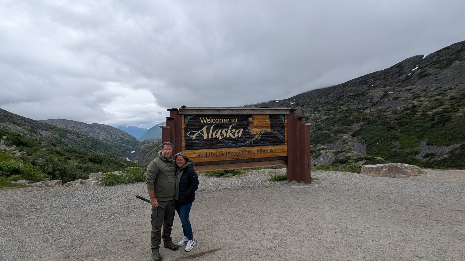 Travelers at the Welcome to Alaska sign in the Klondike mountains